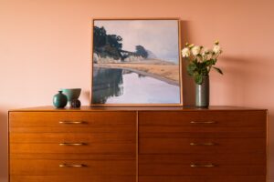 a sideboard with a painting, vase of flowers and ceramics