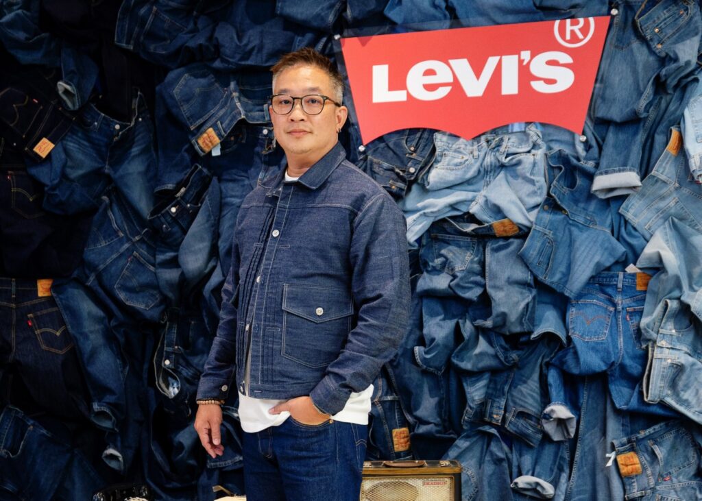 man standing in front of a heap of blue jeans trousers