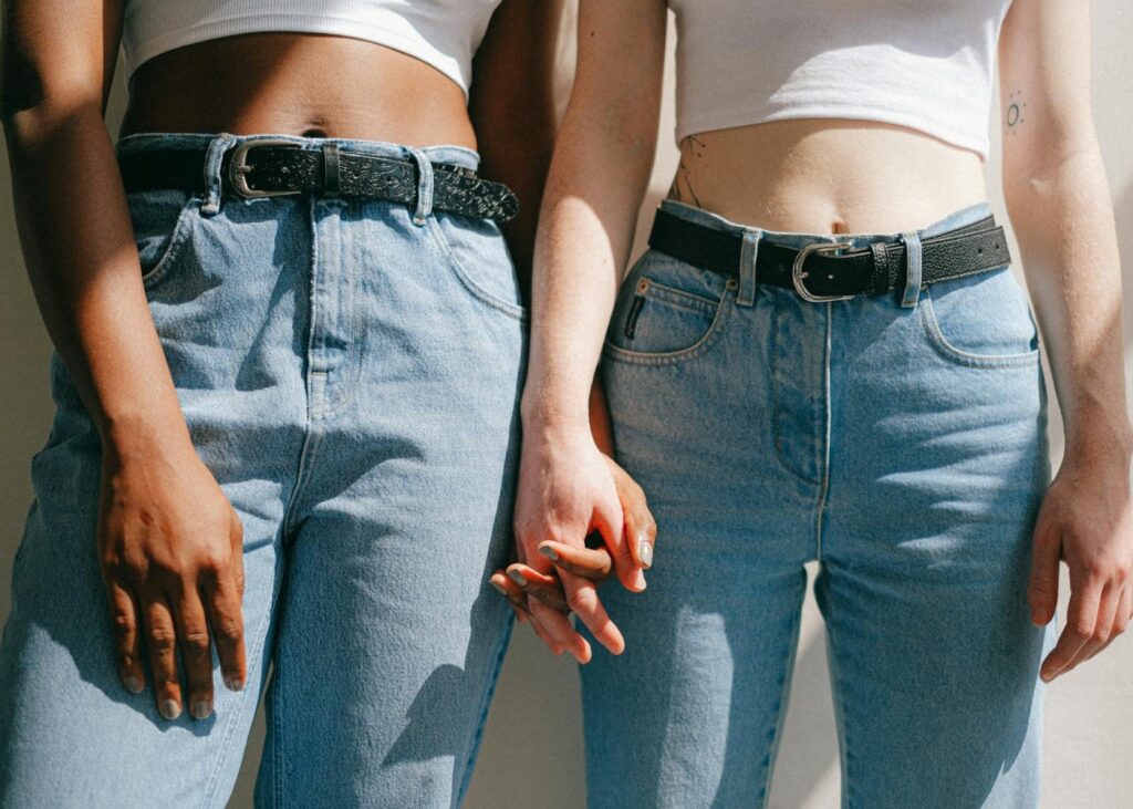 two women wearing blue jeans and white tank tops